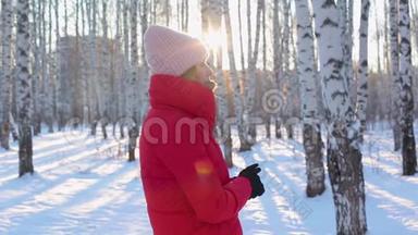 穿着红色冬衣的可爱的年轻女子站在<strong>画报</strong>城市公园里，在寒冷的阳光明媚的日子里有桦树，在期待中结冰